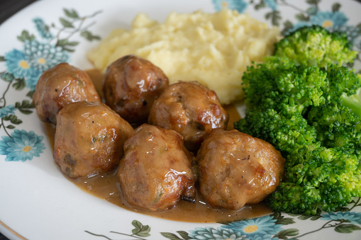 A plate of meatballs covered in thick sauce served together with mashed potato and broccoli.