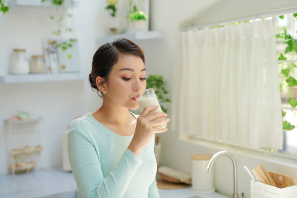 joven sedienta bebiendo leche de un vaso en la cocina - mujer bebiendo leche fotografías e imágenes de stock