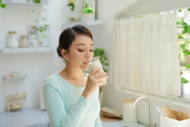 Photo of Thirsty young woman drinking milk from a glass in the kitchen