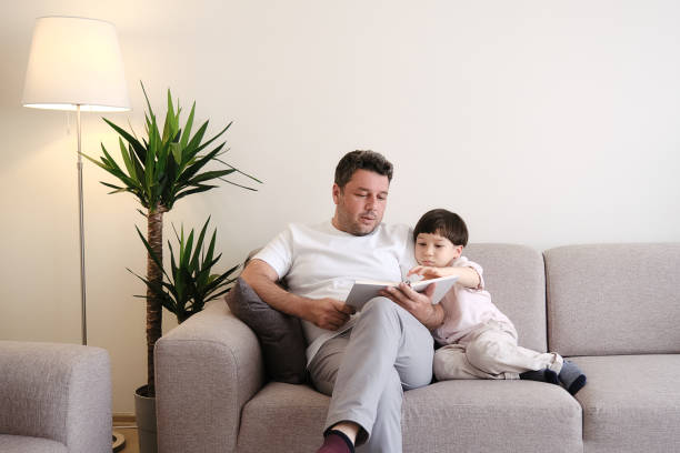 istock Father reading book to son on sofa 1326748380