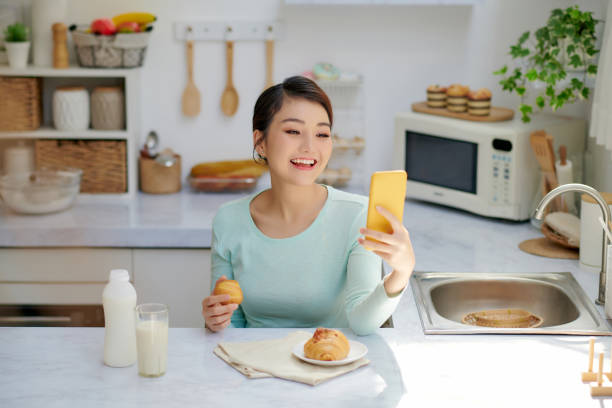 istock beautiful girl using mobile phone while having breakfast at home 1326748569