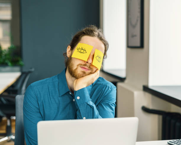 istock Tired sleeping young male office worker hiding eyes with funny sticky notes 1326755360