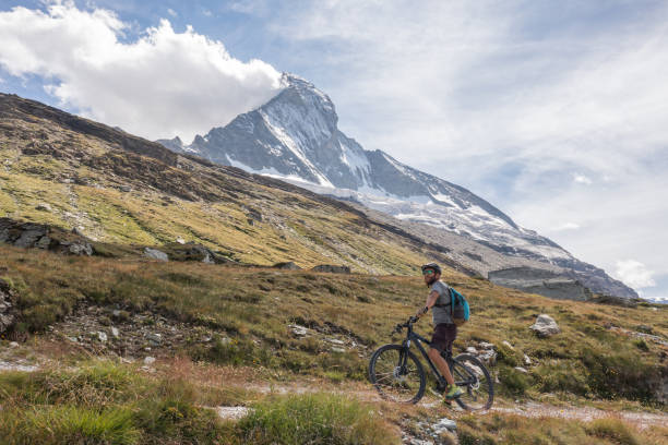 istock Man mountain biker rides along trail below the Matterhorn mountain 1326758617