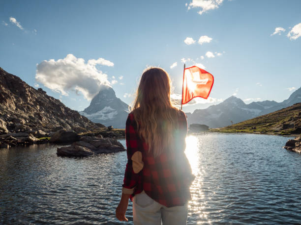 Woman holds Swiss flag against mountain landscape, Zermatt Female holding Swiss flag against the mountain landscape with the Matterhorn peak switzerland tourist places stock pictures, royalty-free photos & images