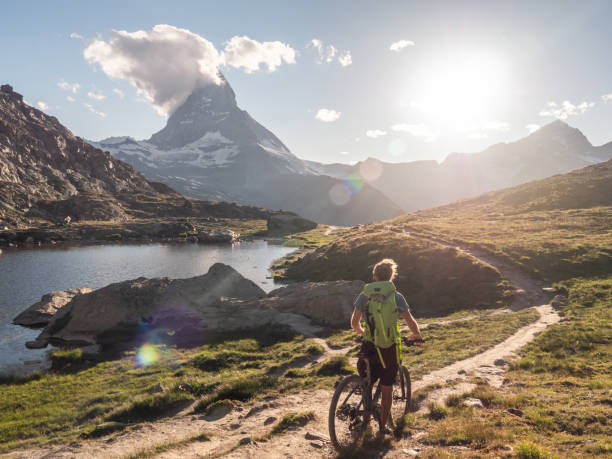 Male mountain biker pauses to look at the Matterhorn mountain Matterhorn mountain peak in distance and layers of clouds matterhorn stock pictures, royalty-free photos & images