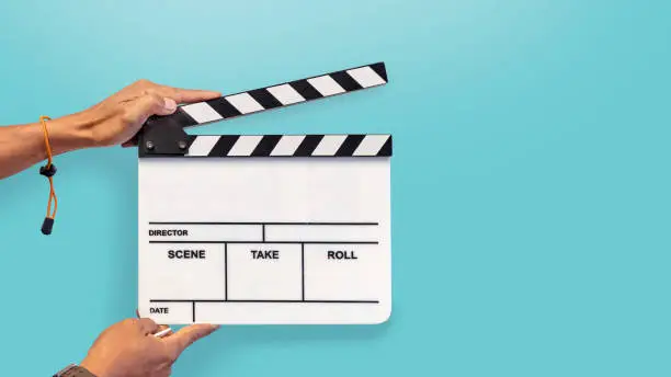 Photo of Hands with a movie clapperboard on blue background