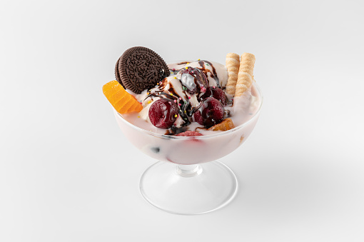 ice cream bowl with fresh frozen yogurt, fruits, cookies and cherries isolated on a white and gray background with natural shadows