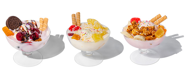 many ice cream bowls with fresh frozen yogurt, fruits, cookies and cherries isolated on a white background with hard shadows