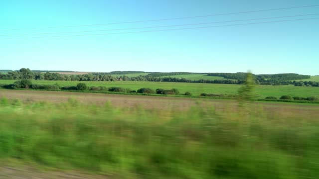 View from car window of green countryside fields and clear blue sky in summer sunny day. Trip, travel, journey by car. Transport