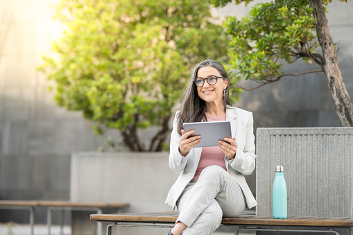 pretty mature business woman with tablet and glasses sitting on a bench