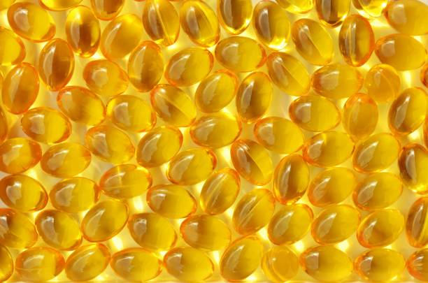 Vitamin D capsules close-up as a yellow background on a full frame Vitamin D capsules close-up as a yellow background on a full frame. Pharmacy industry concept. drug manufacturing stock pictures, royalty-free photos & images