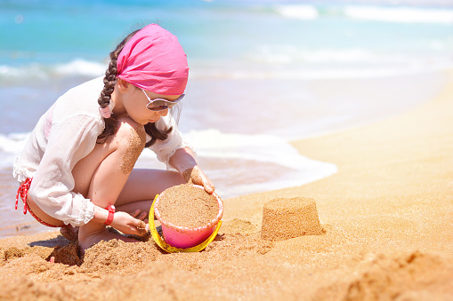 A beautiful little girl builds sand towers on the beach near the sea. Family beach leisure and vacation concept