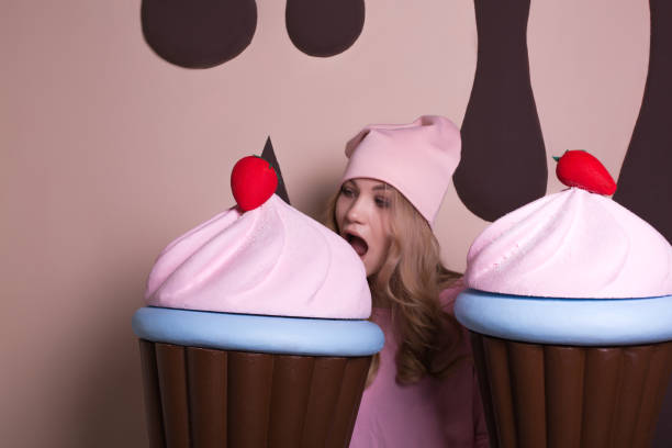 istock Hungry blonde girl wearing pink cap biting big cupcake at studio 1326778901