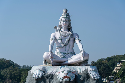 Statue of meditating Hindu god Shiva against the blue sky on the Ganges River at Rishikesh village in India, close up