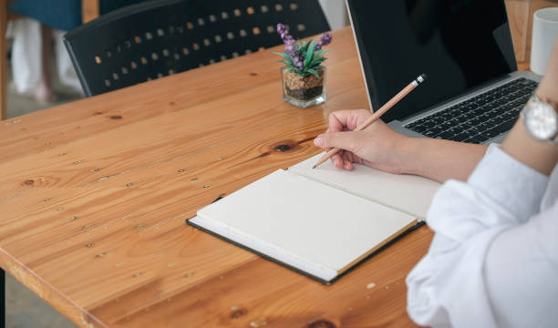 istock woman hand writing on notebook with pencil while sitting at the table in modern office. 1326781160
