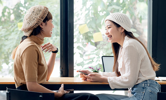 Two young asian woman talking together with happiness while sitting at cafe.
