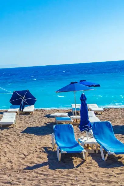 Relax on blue sun loungers at vacation in Rhodes Greece with beautiful clear turquoise waters of amazing Elli beach.