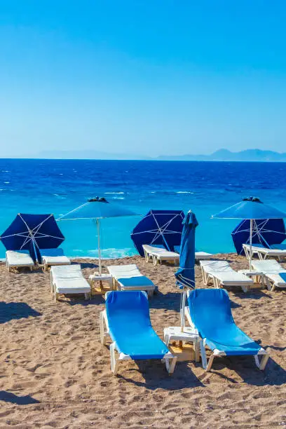 Relax on blue sun loungers at vacation in Rhodes Greece with beautiful clear turquoise waters of beautiful Elli beach.