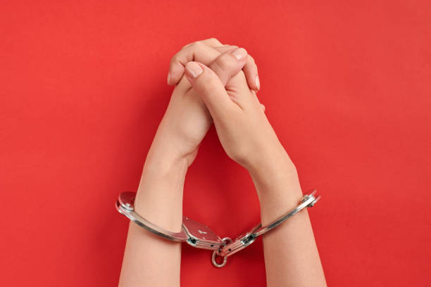 istock Crossed hands in handcuffs on red background 1326784675