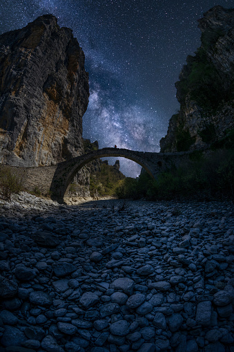 Beauty in Nature at night. Nightscape of the millions of stars in the dark blue sky over the silhouette of a person at a Roman bridge at the edge of the cliffs. Outer space and Astronomy.