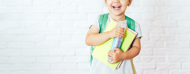 Child with green backpack holding school supplies.