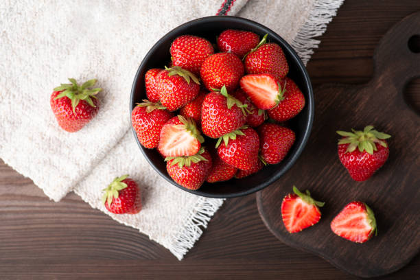 Top-down photo of many strawberries on dark table with a white natural linen towel in the corner stock photo