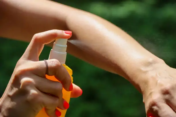 Insect repellent against mosquitoes, ticks. Skin protection against tick and other insect. Bug spray anti insects. Woman spraying insect repellent using yellow spray bottle.