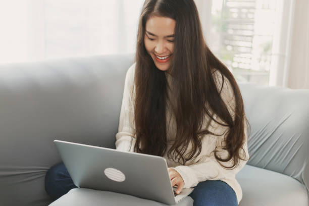 istock Young happy attractive Asian wearing casual clothes using laptop computer and relax sitting on couch sofa at home. Asian using internet working online . Online job hunting concept 1326791616