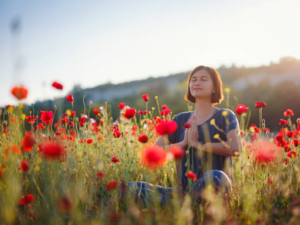 美しい女性は日没時にケシのフィールドで瞑想 - field poppy single flower flower ストックフォトと画像