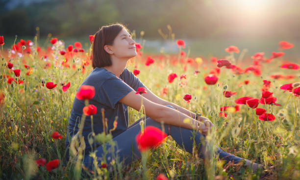 una hermosa mujer medita en un campo de amapolas al atardecer - conciencia plena fotografías e imágenes de stock