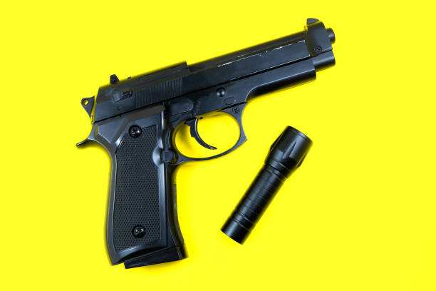 istock Black gun and flashlight lies on a yellow background. Private detectives work. Searching information concept. 1326801913