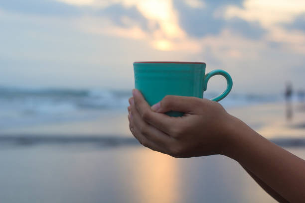 istock A cup of coffee in hands on beach background at sunset. 1326815327
