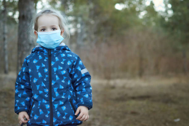 Little girl with protective mask looking in front in park outdoor walk in forest stock photo