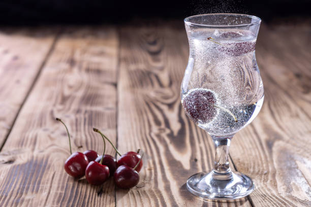 un bicchiere di acqua frizzante fresca con una ciliegia su uno sfondo di legno - soft cider foto e immagini stock