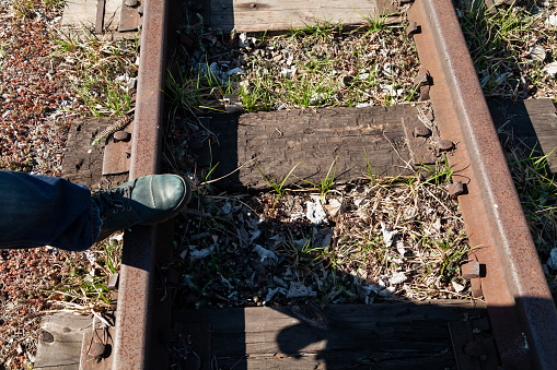left foot in the boot stands on the rail of a narrow-gauge railway track. Green grass grows between the sleepers