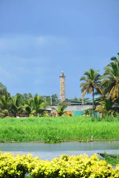 Grand-Bassam, Aboisso department, Sud-Comoé region, Comoé district, Ivory Coast / Côte d'Ivoire: wetlands of the Ébrié lagoon and colonial lighthouse completed in 1914, round masonry tower, typical of the military architecture of the time - deactivated in 1951 with the opening of the port of Abidjan and the new lighthouse of Port-Bouët - UNESCO world heritage site -  'le phare' - seen from Quartier France -  Historic Town of Grand Bassam, first capital of the Ivory Coast.