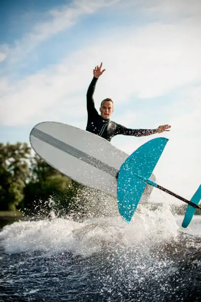 beautiful close-up view of foilboard on which man in black wetsuit is effectively jumping on the wave