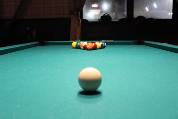 Billiard snooker pyramid on green table. American billiards pool on a green table. Sports game of billiards on a green cloth. Multi-colored billiard balls with numbers, cue, on a pool table. Gambling game of Billiards at bar evening, nightlife