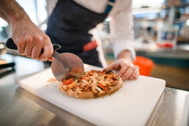 close-up of pizza on cutting board that chef cuts into pieces with cutter close-up of small round pizza on cutting board that man chef neatly cuts into pieces with pizza cutter pizza cutter stock pictures, royalty-free photos & images