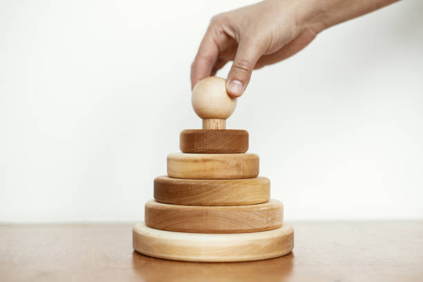 istock Hand holding natural wooden pyramid ring on table on white wall background. Eco friendly plastic free modern toys for toddler. Montessori education and play. Stylish simple wooden toy for child 1326835673