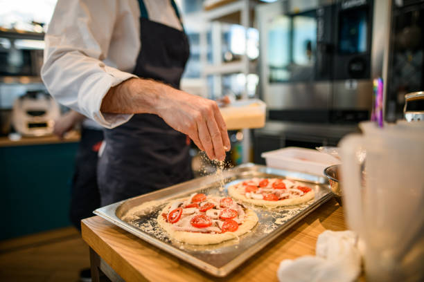 istock pizzas lie on baking sheet and male chef gently sprinkles grated cheese on its 1326836517