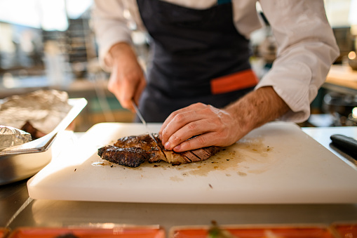 male chef skillfully cuts a fried piece of meat on a cutting board. Close-up view