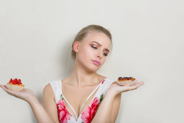 Upset dieting blonde girl looking on sweet cream desserts in her hands. Space for text