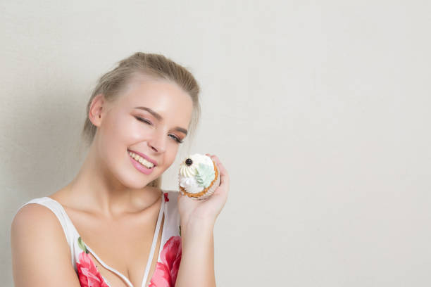 Cool winking blonde woman with perfect makeup holding sweet cream dessert. Space for text