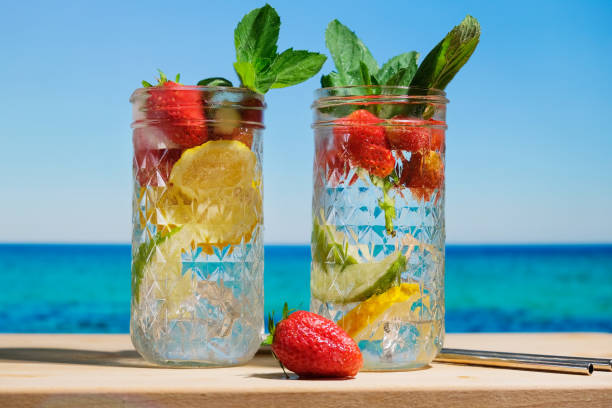 Hard seltzer cocktails, blue sea on background Hard seltzer cocktails with strawberry, lemon and mint. Alcoholic cocktails on summer beach bar. Sea resort concept. soda water glass lemon stock pictures, royalty-free photos & images