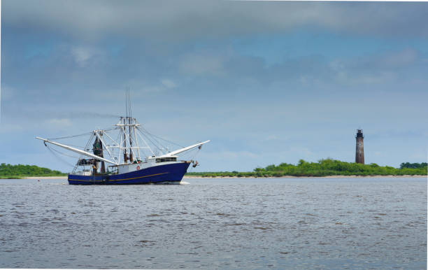 una barca di gamberetti passa lo storico faro di sabine pass - barca per pesca di gamberetti foto e immagini stock