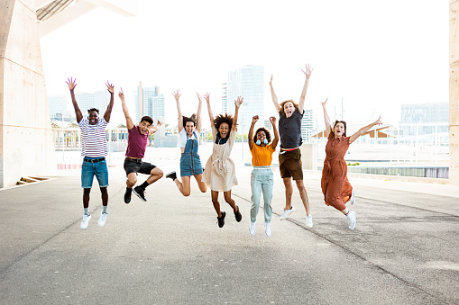 Happy multiracial people jumping together outdoors - Friendship concept with group of young friends from diverse cultures and races having fun with city background
