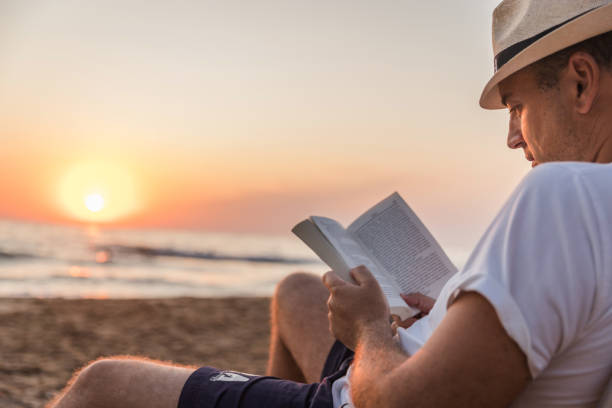 hombre leyendo un libro en la playa - mid adult men smart casual white happiness fotografías e imágenes de stock