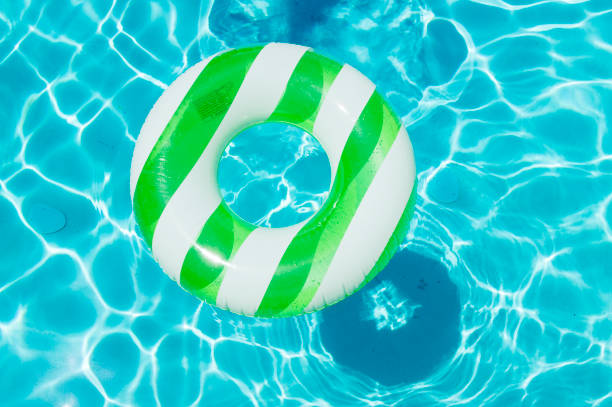 This bright striped float ring is sitting on the surface of clear blue water in a swimming pool.  Sunlight bouncing from the water's surface is seen reflecting on the bottom of the pool.  The ring's shadow is seen at one corner of the picture reflecting from the bottom of the pool.