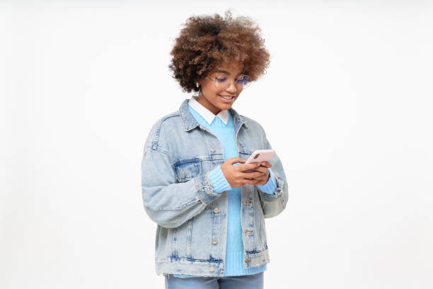 side portrait of smiling african american girl with afro hairstyle, glasses and earphones holding phone, chatting with friend, using social media app, isolated on gray background - teenager teenagers only one teenage girl only human face imagens e fotografias de stock